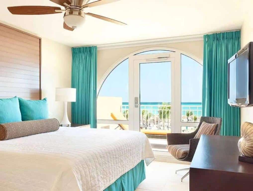 Quarto do Bluegreen at La Cabana Beach Resort & Casino. Uma cama de casal do lado esquerdo, do lado direito uma raque com uma televisão e uma poltrona. No fundo a porta da varanda com vista para a praia.