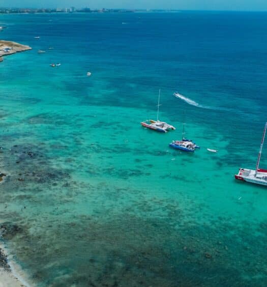 Imagem da praia de Boca Catalina durante o dia com mar do lado direito da imagem com barcos navegando nas aguas e do lado esquerdo faixa de areia. Representa passeios em Aruba.
