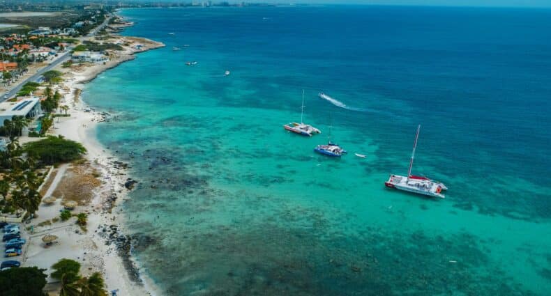 Imagem da praia de Boca Catalina durante o dia com mar do lado direito da imagem com barcos navegando nas aguas e do lado esquerdo faixa de areia. Representa passeios em Aruba.