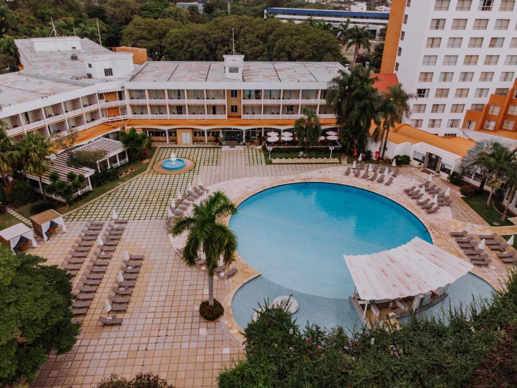 Foto aérea do Bourbon Cataratas do Iguaçu Thermas Eco Resort, mostrando uma piscina redonda grande, coqueiros, espreguiçadeiras e a extensão do hotel.