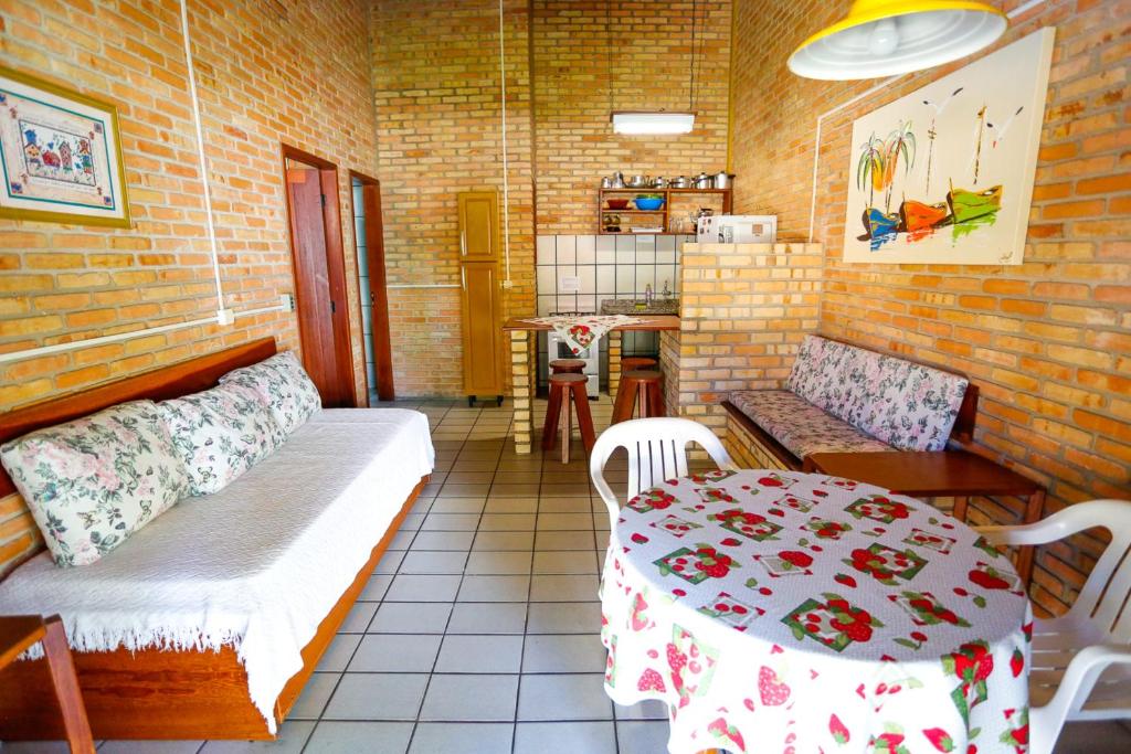 Sala e cozinha do airbnb Cabanas Jurerê. Na frente da imagem, a direita, há uma mesa redonda com duas cadeiras e um sofá com uma pequena mesa ao lado. No lado esquerda há outro sofá e ao fundo está a cozinha.