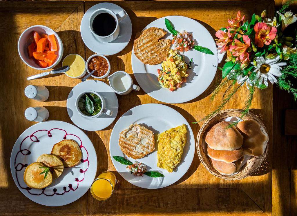 foto de cima de uma mesa de café da amanhã no El Balcón, com três pratos com pães, ovos mexidos e panquecas, além de um cesto de pães e duas xícaras de café e chá de coca.
