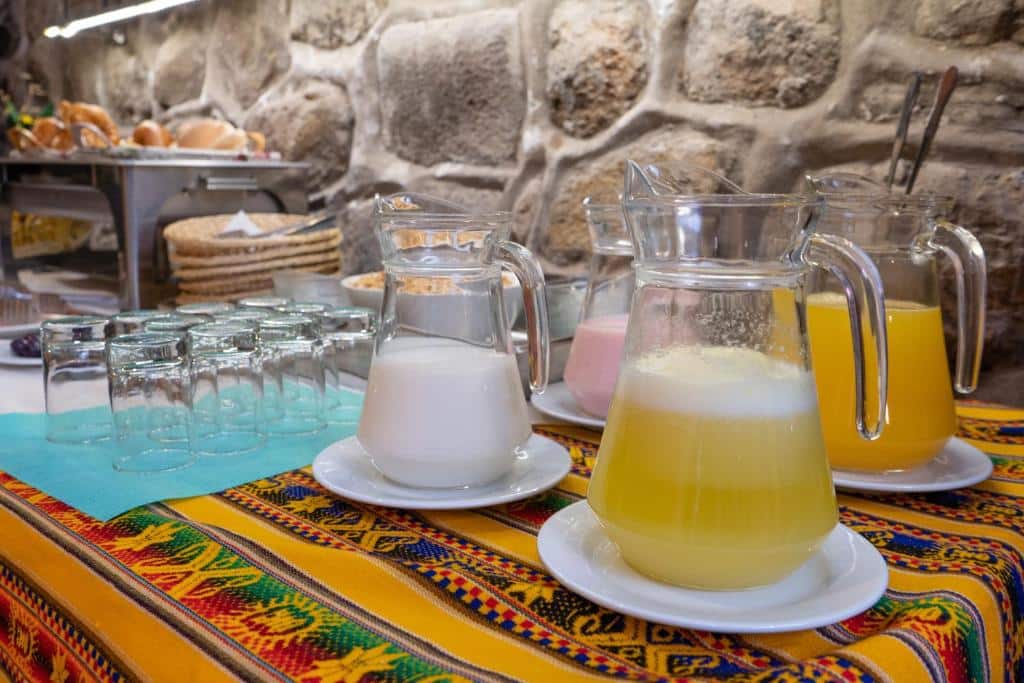 mesa de café da manhã da La Casona Real Cusco com vários copos de vidro e jarras de sucos, leite e yogurte.