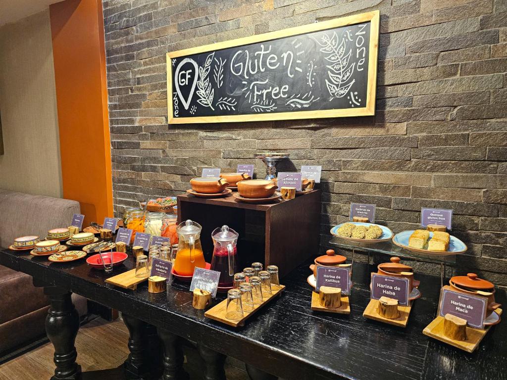 mesa do café da manhã do Sonesta Hotel Cusco com vários pratos e cumbucas de alimentos sem glúten, além de uma grande placa de giz pendurada na parede, acima da mesa, com os dizeres: glúten free