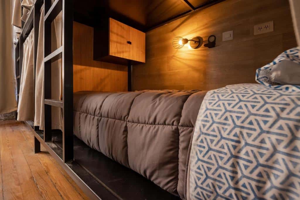 Quarto do Che Juan Hostel BA, um hostel em Buenos Aires, mostrando uma cama bem arrumada e confortável com luminária e armário.