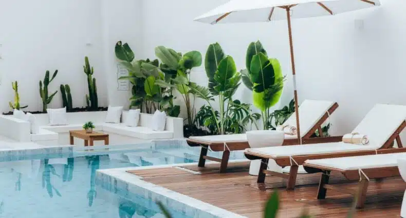 Área da piscina do Olisa Hotel Boutique durante o dia com piscina do lado esquerdo da imagem e do lado direito cadeiras na borda da piscina. Representa hotéis em São Sebastião.