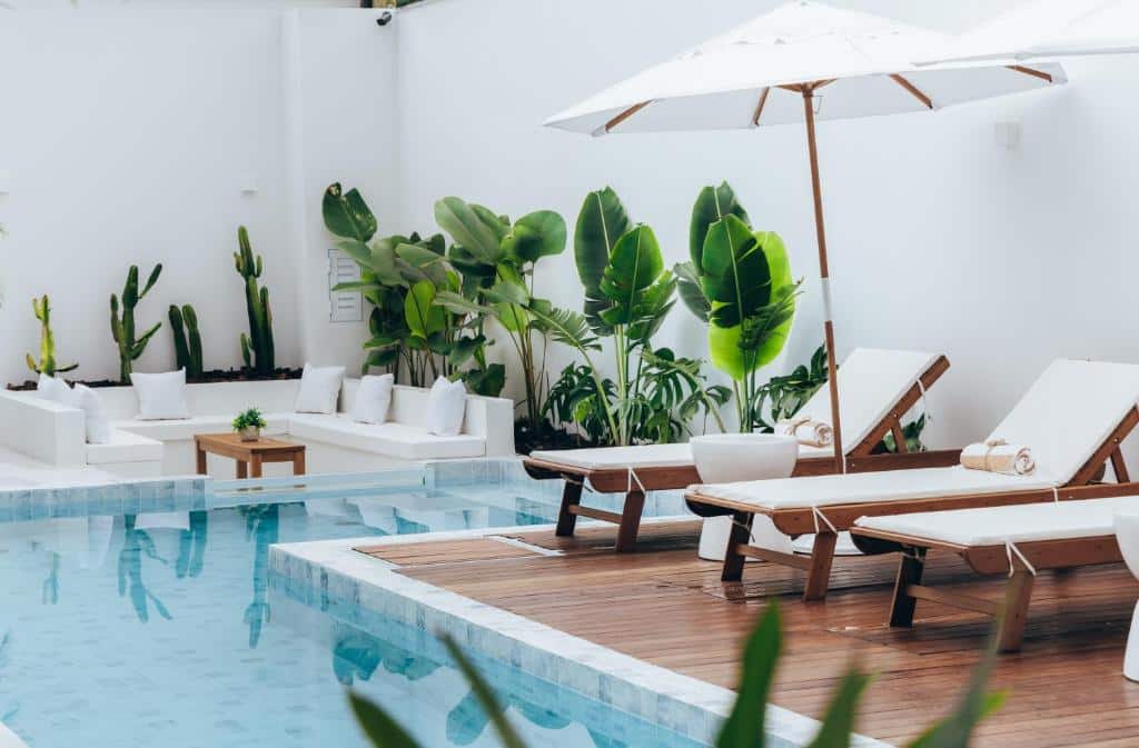Área da piscina do Olisa Hotel Boutique durante o dia com piscina do lado esquerdo da imagem e do lado direito cadeiras na borda da piscina. Representa airbnb em São Sebastião.