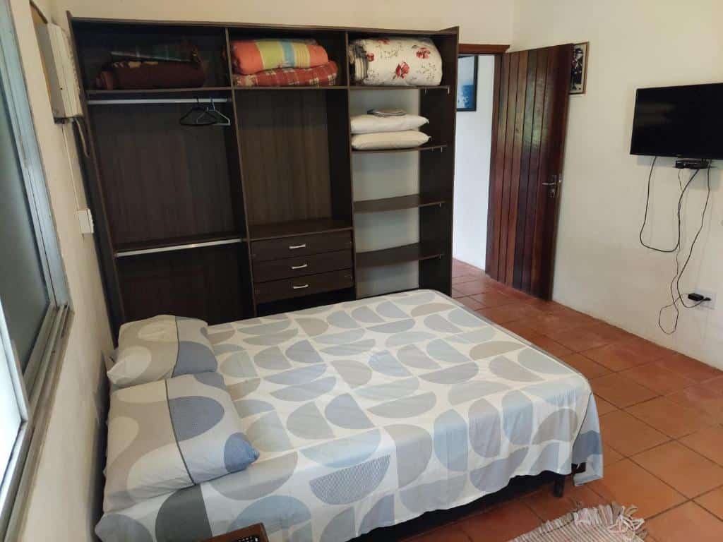 Quarto da Casa a 130 metros da praia de Boiçucanga. Uma cama de casal está de frente para uma tv na parede e ao lado de um grade armário.