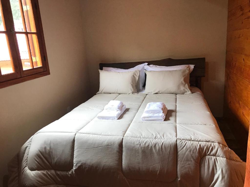 Imagem do quarto em Casa Chalé do Bosque, que está ilustrando o post sobre airbnb em Visconde de Mauá. Há uma cama box de casal no centro, com toalhas em cima. Na sua esquerda há uma janela.