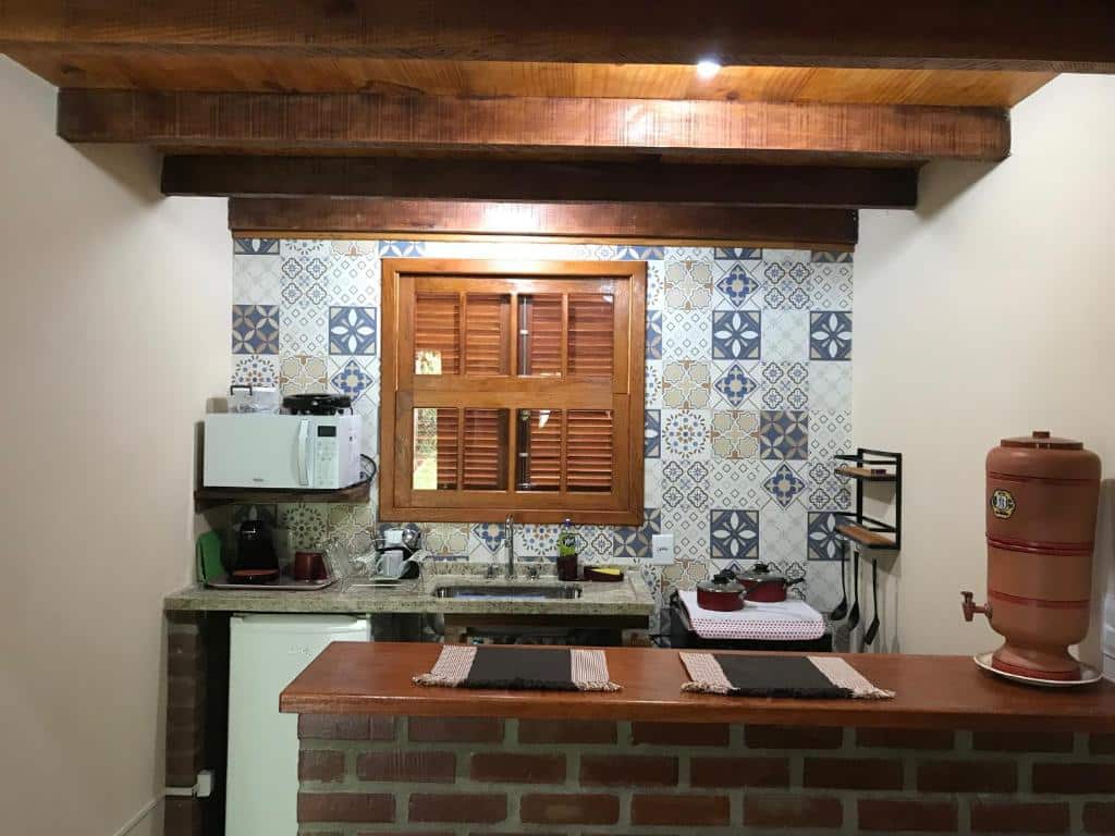 Cozinha na Casa Chalé do Bosque. Há uma bancada com filtro de barro, e a cozinha atrás tem uma pia, fogão quatro bocas, micro-ondas, e frigobar.