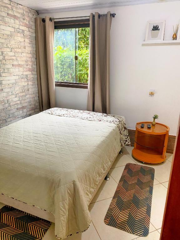 Imagem do quarto em Casa da Lilyan, que está ilustrando o post sobre airbnb em Visconde de Mauá. Há uma cama box de casal à esquerda, atrás dela há uma janela e ao lado direito uma mesa com controle remoto em cima.