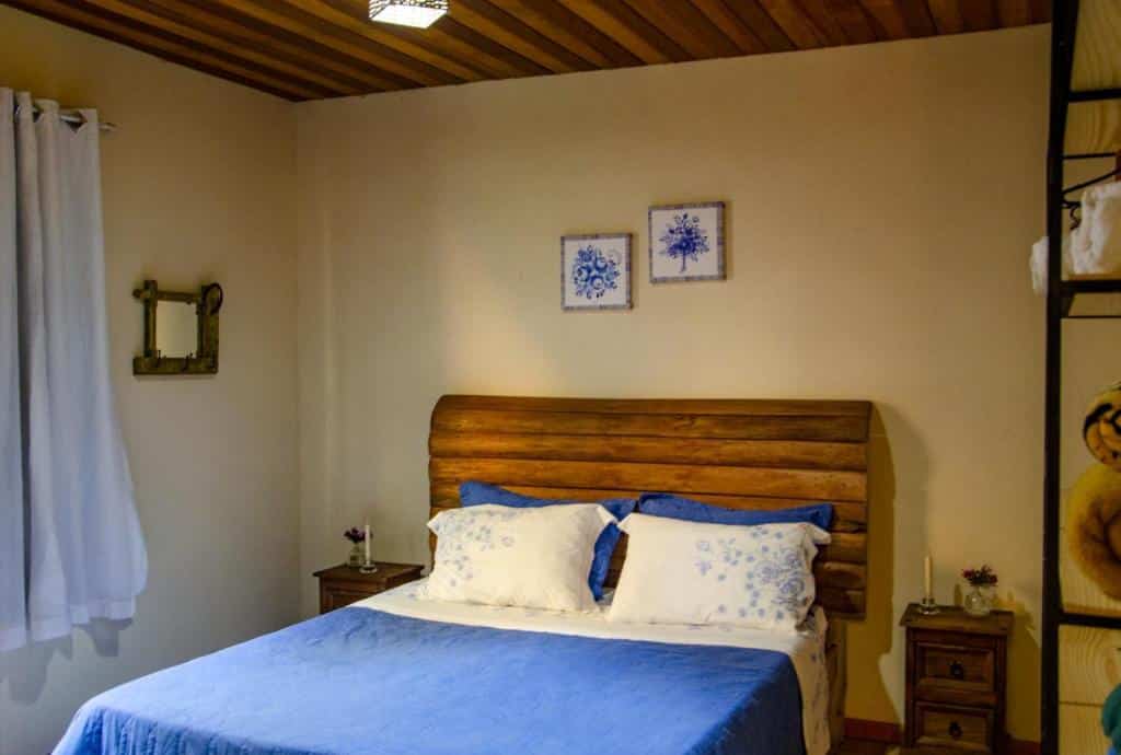 Imagem do quarto em Casa De Férias e Hospedagem Ana Lua, que está ilustrando o post sobre airbnb em Visconde de Mauá. Há uma cama box de casal no centro, e de seus dois lados há uma mesa de cabeceira com gavetas. Na direita também há uma estante com edredons.