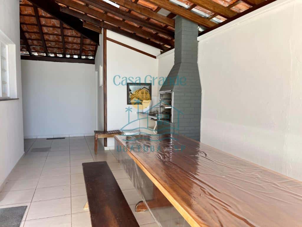 Quintal da Casa Grande Ubatuba. Uma mesa de madeira com bancos do lado direito, atrás uma churrasqueira e uma pia.