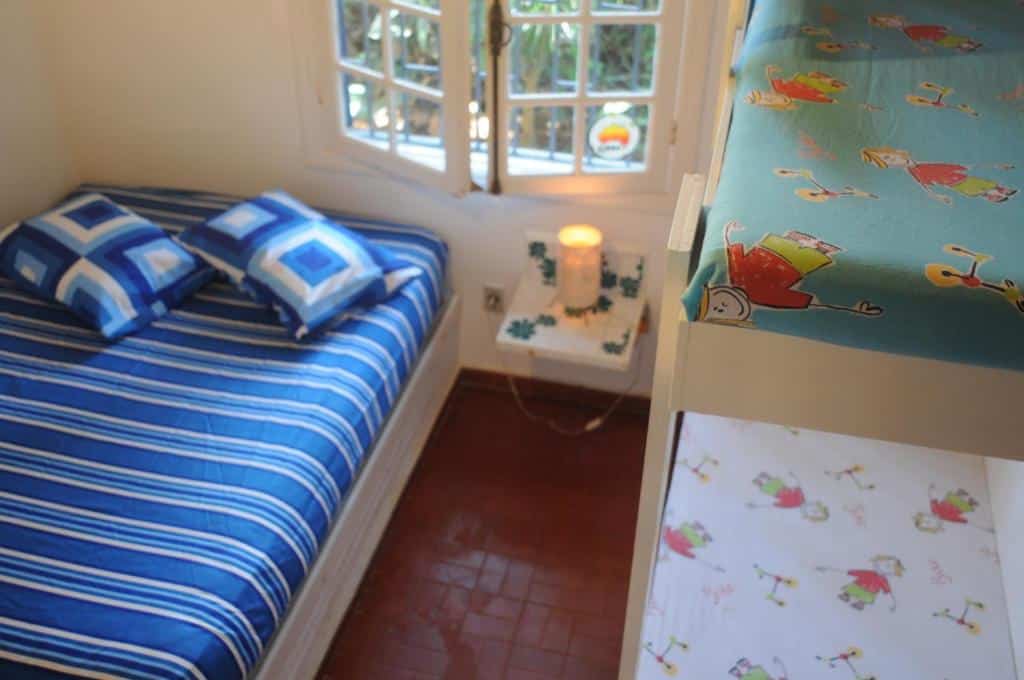 Quarto da Casa na quadra da Praia do Tenório. Do lado esquerdo está uma cama de casal e do lado direito uma beliche. Entre elas há uma prateleira na parede e uma janela.