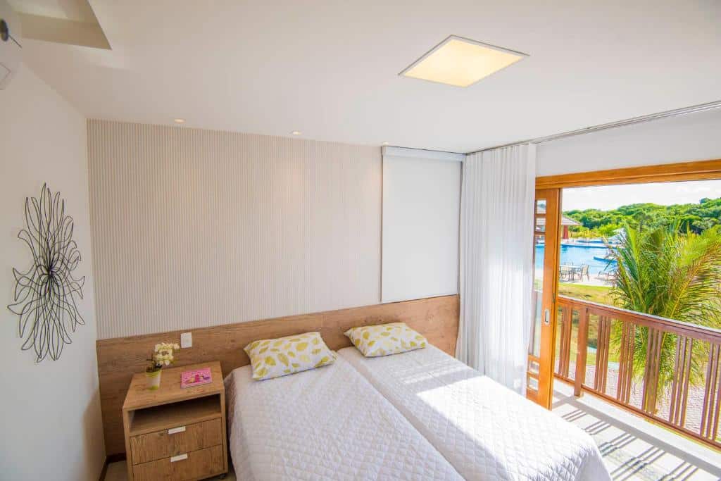 Foto do quarto em Pé na areia - Furstberger, que ilustra o post de airbnb na Praia do Forte. Há uma cama box de casal no centro, e do lado esquerdo dela há uma mesa de cabeceira com gavetas. Na direita há uma varanda espaçosa com vista.