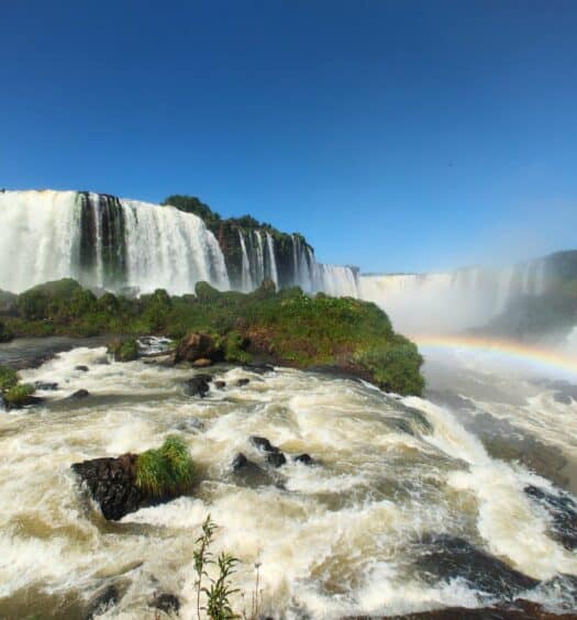 Foto frontal das Cataratas do Iguaçu, onde mostra a queda d'água e um belo arco-íris.