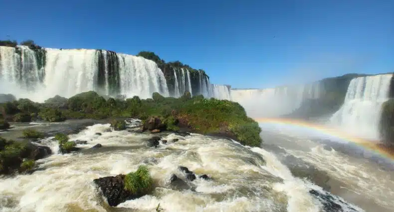 Foto frontal das Cataratas do Iguaçu, onde mostra a queda d'água e um belo arco-íris.