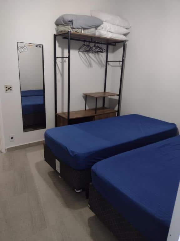 Imagem do quarto do Cello´s Apartamento, ilustrando o post sobre airbnb em Guarujá. Há duas camas box de solteiro, e do lado delas há uma estante com prateleiras e um espelho.