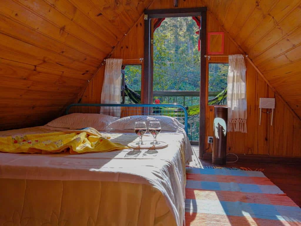Imagem do quarto em Chalé Alto na Montanha, que está ilustrando o post sobre airbnb em Visconde de Mauá. A cama de casal está à esquerda, atrás dela há uma porta de vidro com varanda.
