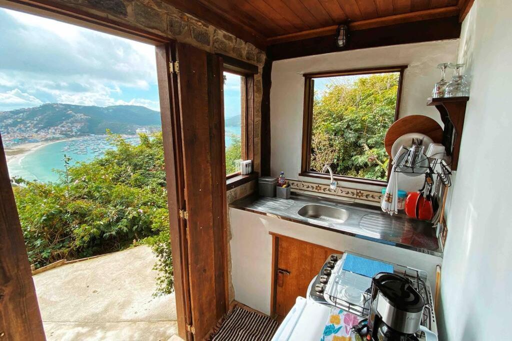 Cozinha do Chalé de Pedras no Pontal do Atalaia. No canto direito da imagem está o fogão, pia e armário da cozinha. Já no canto esquerdo há uma porta aberta com uma vista privilegiada da praia.