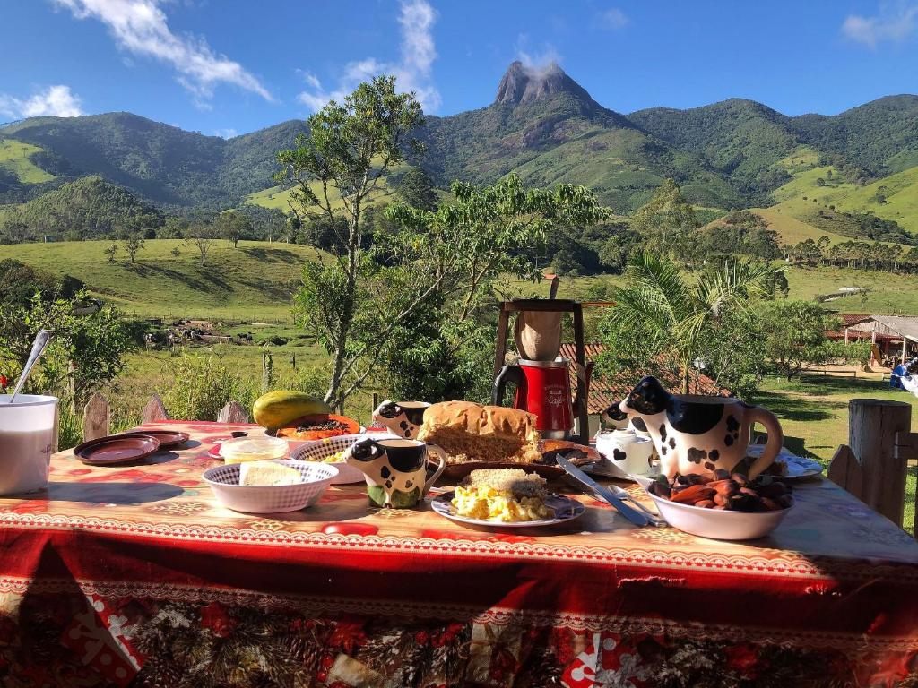 Uma mesa posta com um café da manhã extenso ao ar livre com vista para as montanhas no Chalé jeito de roça na Pedra Selada.