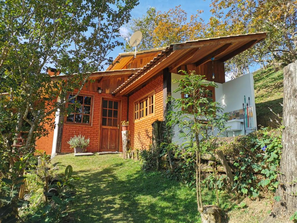 Exterior do Chalé Mauá Conforto e Arte. Há um gramado verde com árvores e o chalé está no meio. Possui uma lavanderia com tanquinho na direita.