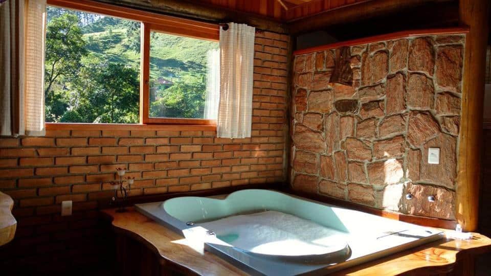 Imagem do Chalé Truta da Floresta, que está ilustrando o post sobre airbnb em Visconde de Mauá. Há uma banheira de hidro dentro do chalé, e de frente para ela há uma janela com vista.