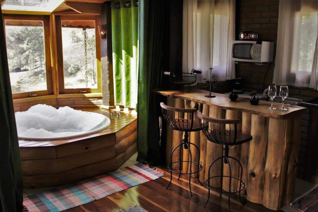 Chalés de Analuz. Há uma banheira hidro na esquerda, de frente para janelas, e na direita há uma mini cozinha com bancada.