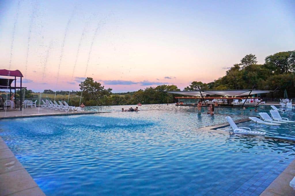 Foto do Complexo Eco Cataratas Resort, mostrando a piscina do resort, com pessoas dentro. Há um quiosque no fundo à direita dentro da piscina.