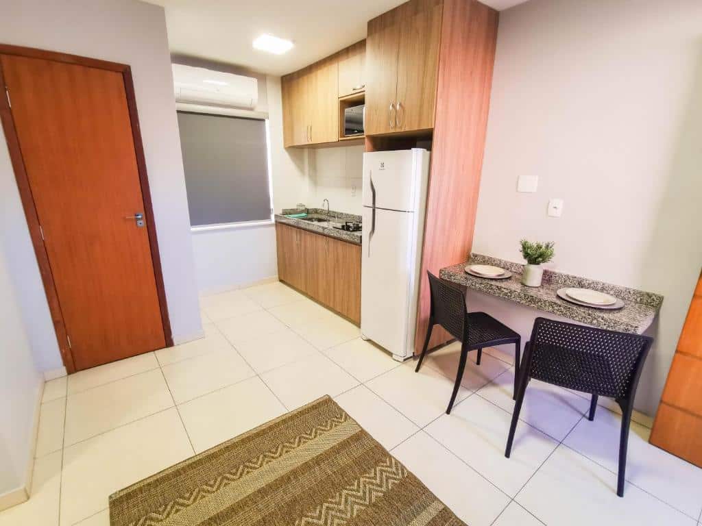 Cozinha do Ap Centro com duas cadeiras e uma banqueta de mármore do lado direito da imagem e do lado esquerdo uma cozinha com armário, pia e geladeira.