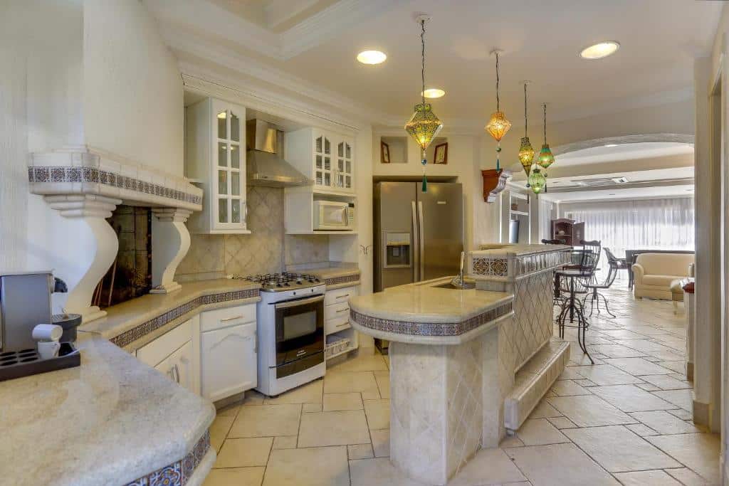 Cozinha do airbnb Villas Jurerê Residences. A esquerda da cozinha há vários armários, com um fogão entre eles, no lado direito há uma geladeira e no meio da cozinha há uma bancada. Mais ao fundo há uma abertura que vai para a sala.