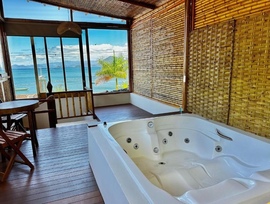 Parte do Deck Da Villa Resort que mostra uma banheira de hidromassagem em um espaço com paredes de bamboo e paredes de vidro com vista para o mar. Imagem ilustrando post Airbnb em Picinguaba.