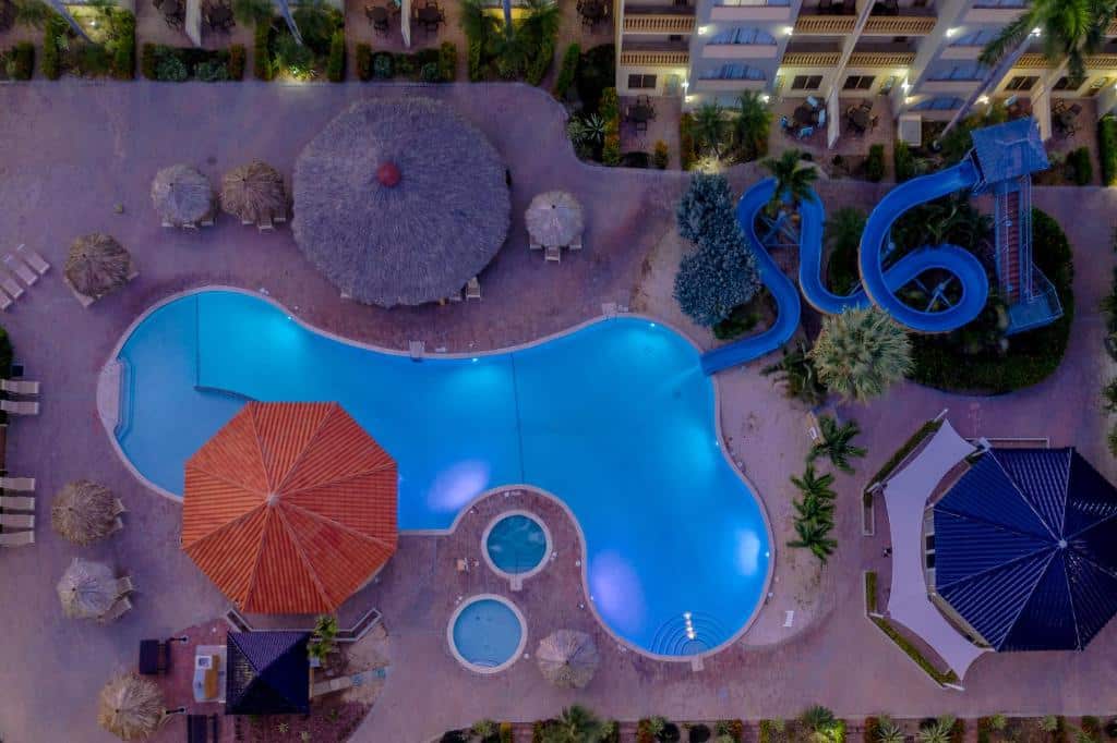 Área externa do Eagle Resort. No meio uma piscina com tobogã. No fundo o hotel ao redor da piscina guarda-sóis.