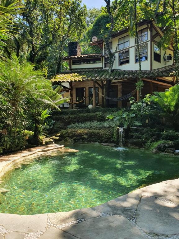 Frente da Casa Rio- Mar durante o dia com um rio a frente e ao fundo a residência. Representa airbnb na praia do Engenho.