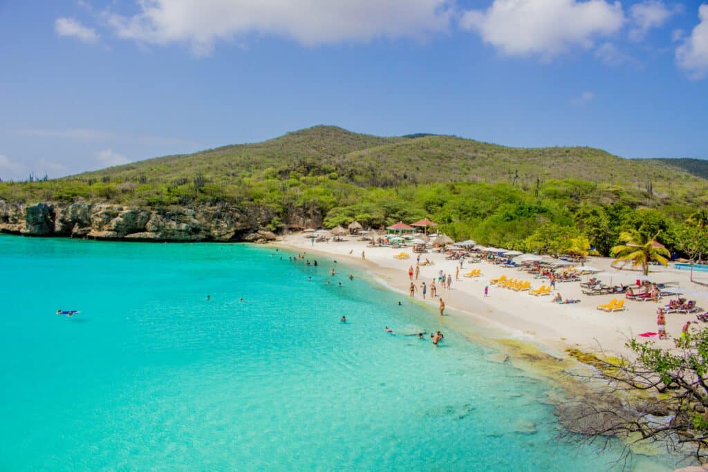 Imagem da praia de Grote Knip em Curaçao durante o dia com mar do lado esquerdo da imagem e do lado direito faixa de areia com alguns banhistas.