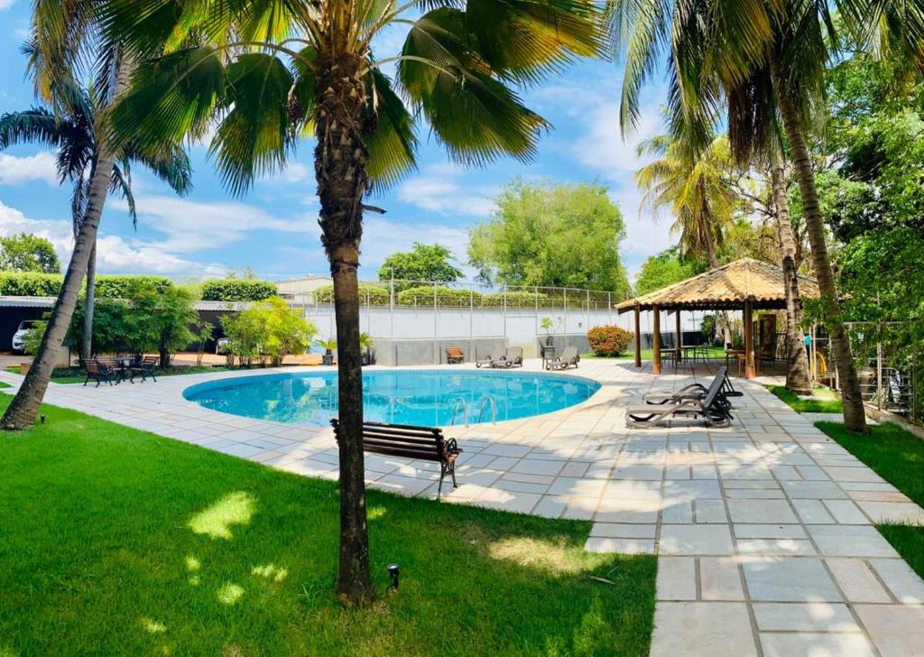 Área externa do Hotel Beira Rio. No meio uma piscina aor ar livre, ao redor cadeiras de tomar sol, bancos de madeira e um jardim com palmeiras. No fundo, no lado direito um quiosque.