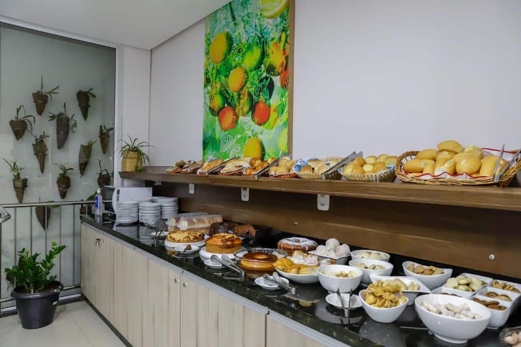 Parte do Hotel Trevita Foz que mostra uma bancada com armário e uma prateleira e ambas com pães, bolos e doces de café da manhã. Imagem ilustrando post Hotéis em Foz do Iguaçu.