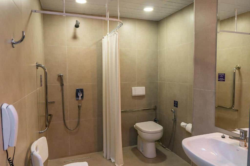 Banheiro do ibis budget Foz do Iguaçu que mostra os recursos de acessibilidade para pessoas com mobilidade reduzida, como barras de apoio, vaso sanitário elevado , cadeira e interfone. Imagem ilustrando post Hotéis em Foz do Iguaçu.