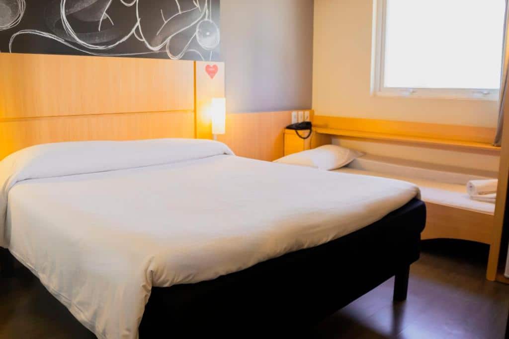 Foto do quarto do Ibis Foz do Iguaçu, ilustrando o post sobre Onde ficar em Foz do Iguaçu. Na esquerda há uma cama box de casal, e do seu lado direito há uma janela.