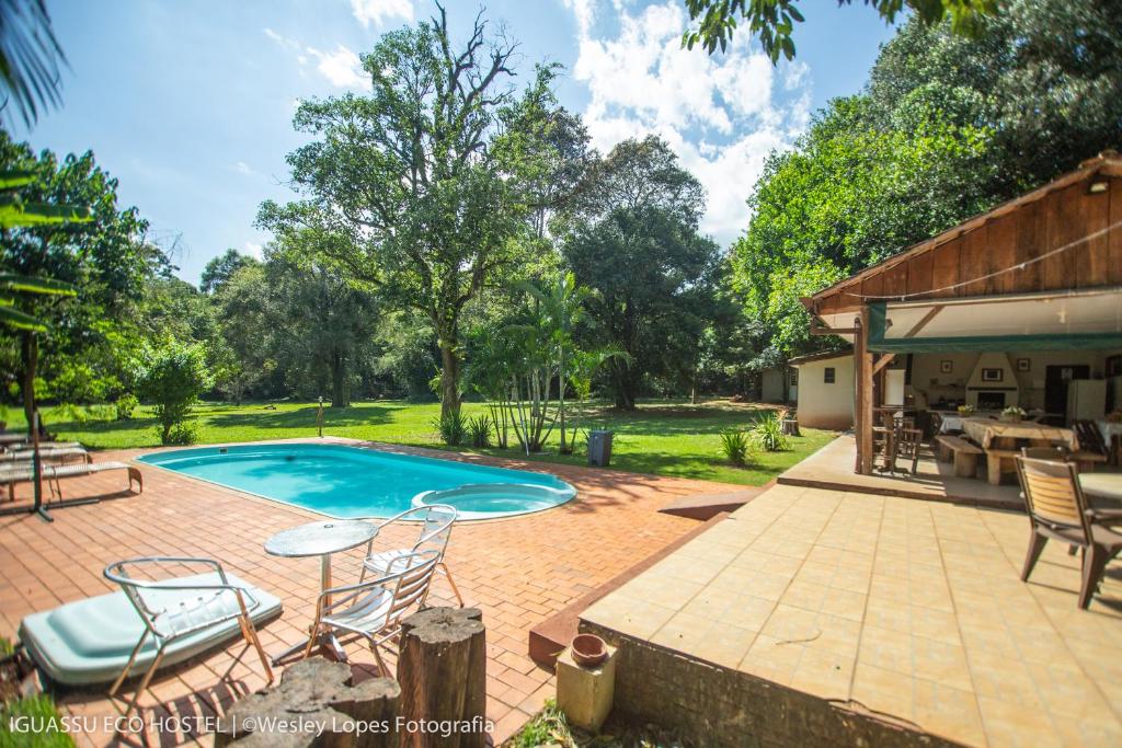 Foto do Ibis Foz do Iguaçu, mostrando a área externa do hostel com um quiosque à direita com mesas e churrasqueira, e piscina na esquerda, com espreguiçadeiras e um jardim cheio de árvores.