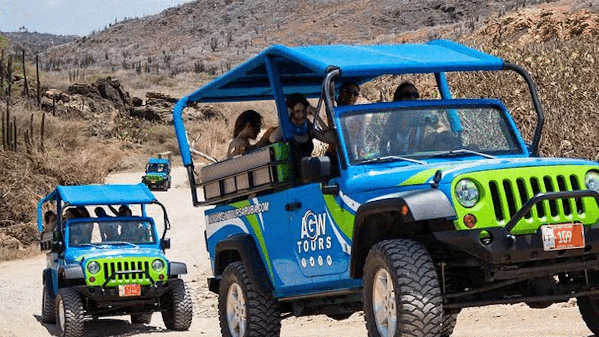 Imagem de dois jipes uma frente e outro atrás andando durante o dia em Aruba com pessoas dentro. Representa praias em Aruba.