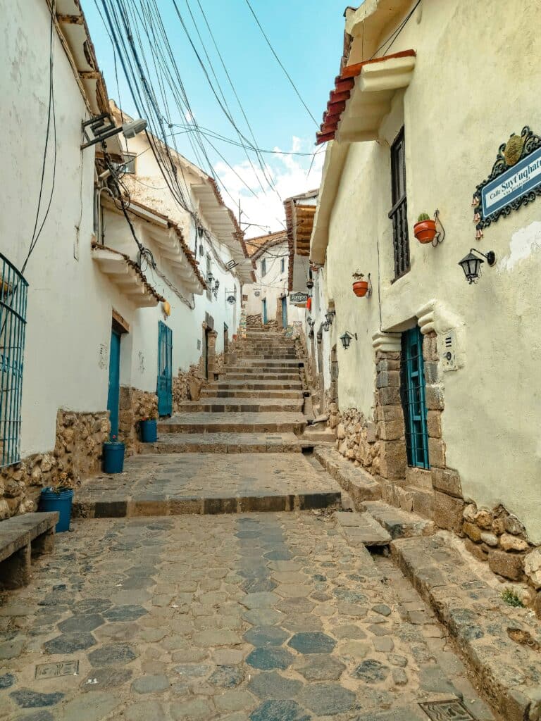 ruas de pedra em uma das ladeiras antigas da região de san blas, em cusco. Dos dois lado da rua há casas com portas na cor azul.