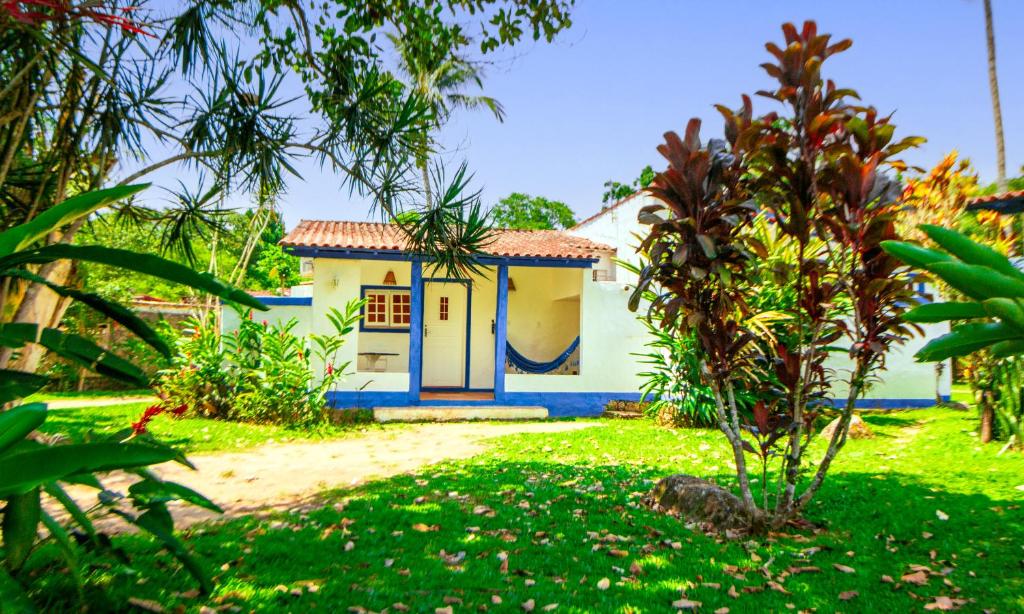 Área externa da VELINN Pousada Bromelias. Há uma grande faixa de grama com muitas plantas e árvores, há também um caminho que vai para um chalé ao fundo,onde há uma rede na varanda.