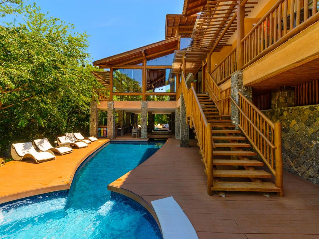 Área externa do Kalango Hotel Boutique. No lado direito da imagem há uma escada de madeira que dá acesso ao hotel. No lado esquerdo há uma piscina no meio de uma estrutura de madeira. Ainda no lado esquerdo estão cinco espreguiçadeiras e grandes arbustos.