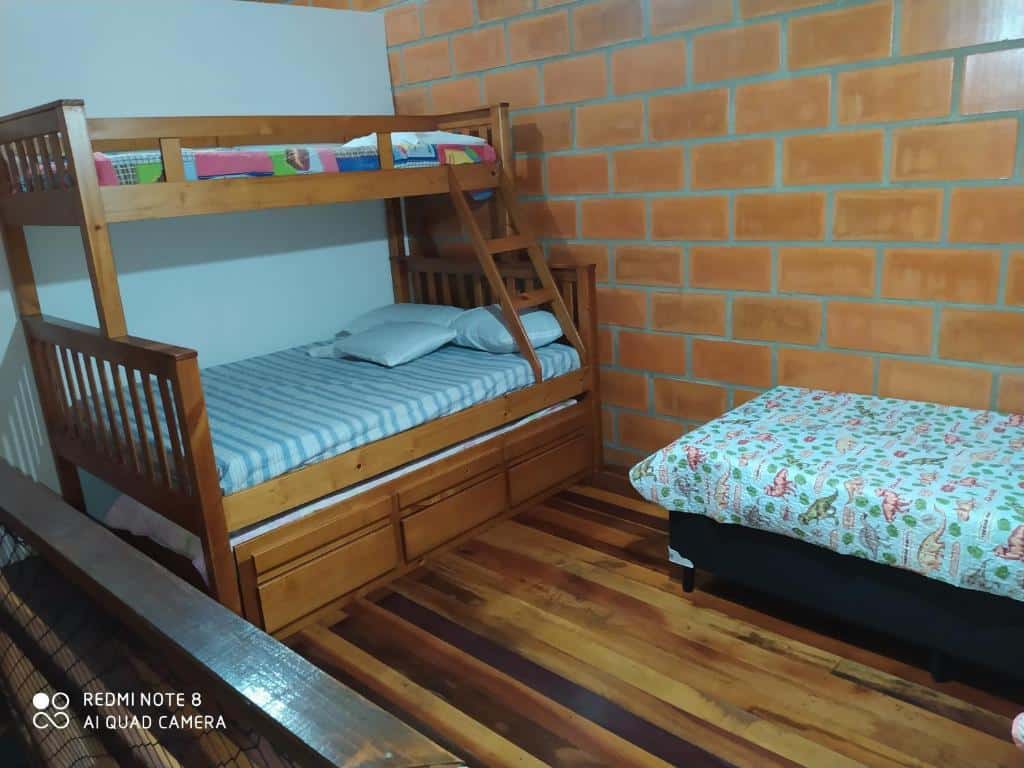 Um dos quartos do Maranduba Ville II. Uma cama beliche está do lado esquerdo, de frente para uma cama de solteiro do lado direito. O chão é todo de madeira e a parede de tijolos.
