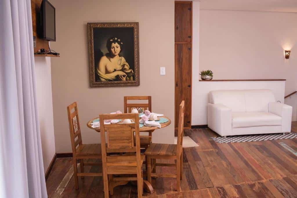 Sala de estar do Loft Sopro da Serra com mesa de jantar do lado esquerdo da imagem com mesa redonda e quatro cadeiras e do lado direito ao fundo um sofá.