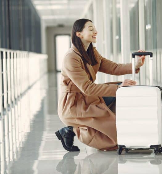 Uma mulher em um corredor de um aeroporto mexendo em uma mala de rodinhas, para representar seguro bagagem