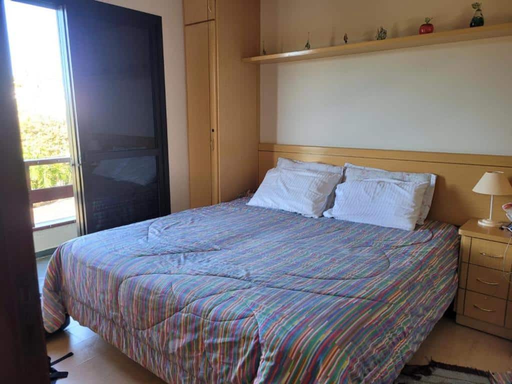 Cama de casal em Piemonte Flat Serra Negra. Há um guarda-roupa com móveis planejados ao redor da cama. Na esquerda dela está a porta para a varanda.