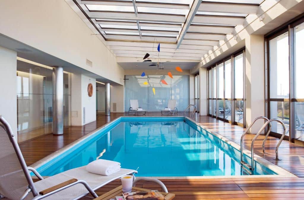 piscina retangular em ambiente coberto com paredes e teto de vidro e espreguiçadeiras no Hotel Madero Buenos Aires
