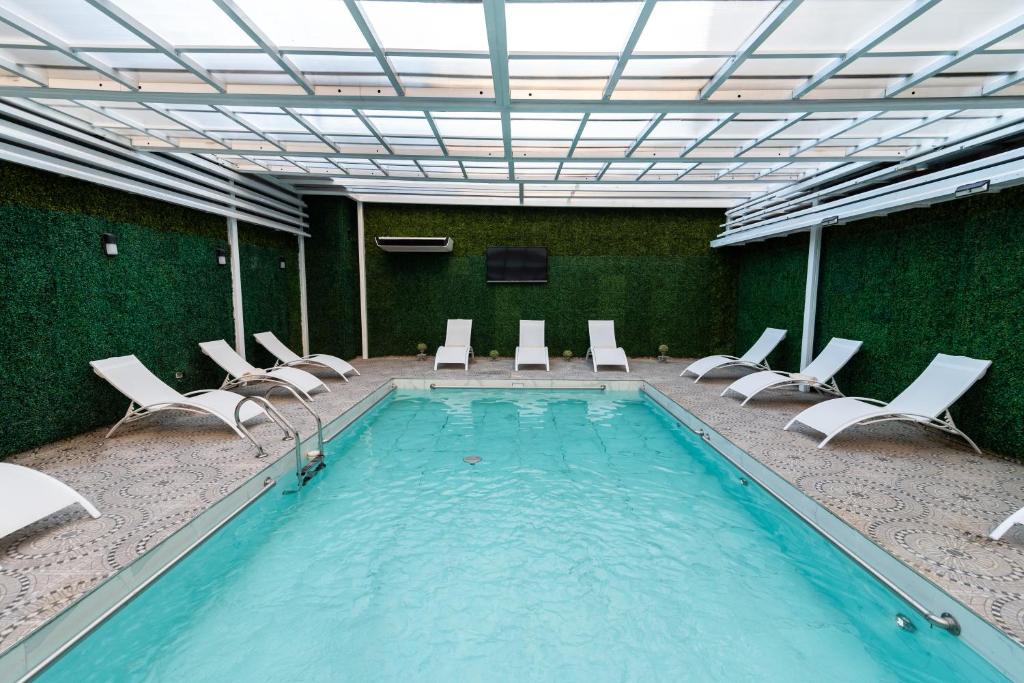 piscina retangular coberta com tetos de vidro e espreguiçadeiras ao redor, nas paredes, há uma textura imitando vegetação no Ker San Telmo Hotel